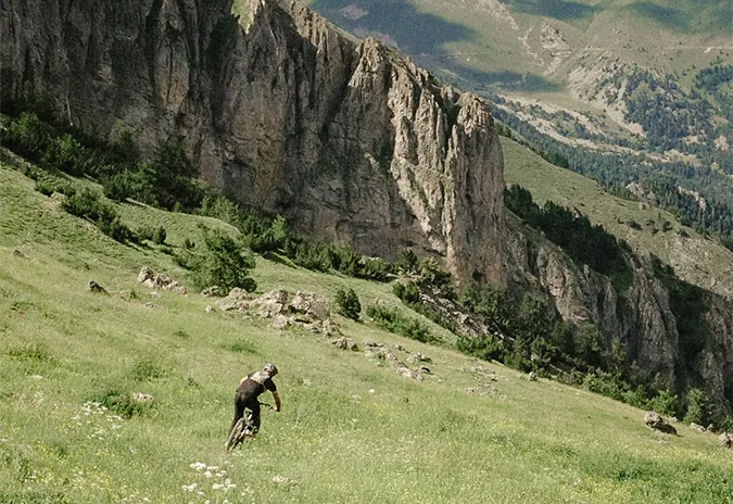 Rider descending a grassy slope beneath limestone cliffs